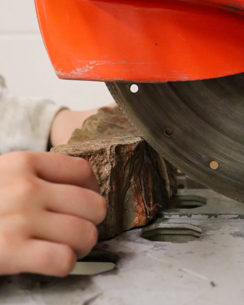 Hands guide a large rock under a saw blade